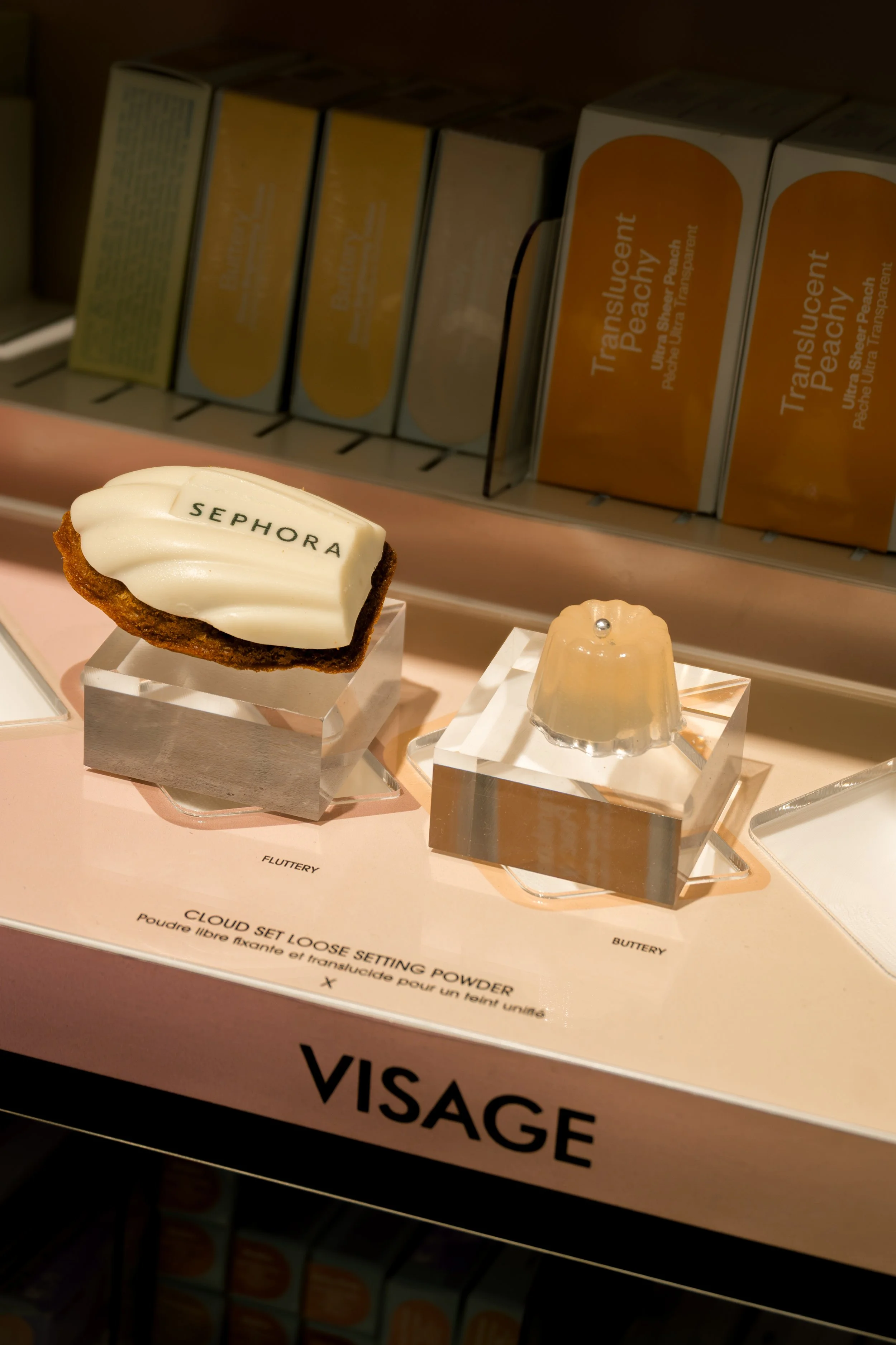 Une vitrine dans un magasin avec des boîtes de crème solaire et des objets de maquillage, dont un gâteau en forme de cachet avec l'inscription "SEPHORA" et d'autres petits objets décoratifs.
