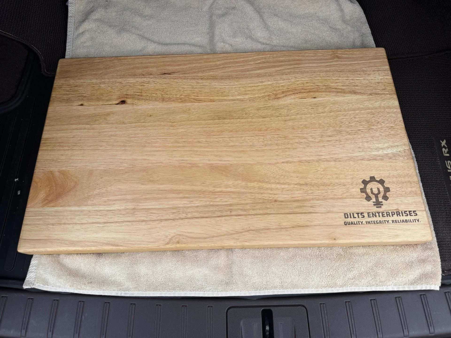 A large wooden box with a logo and text on it, placed on a padded surface, with part of a black object visible at the bottom left corner.