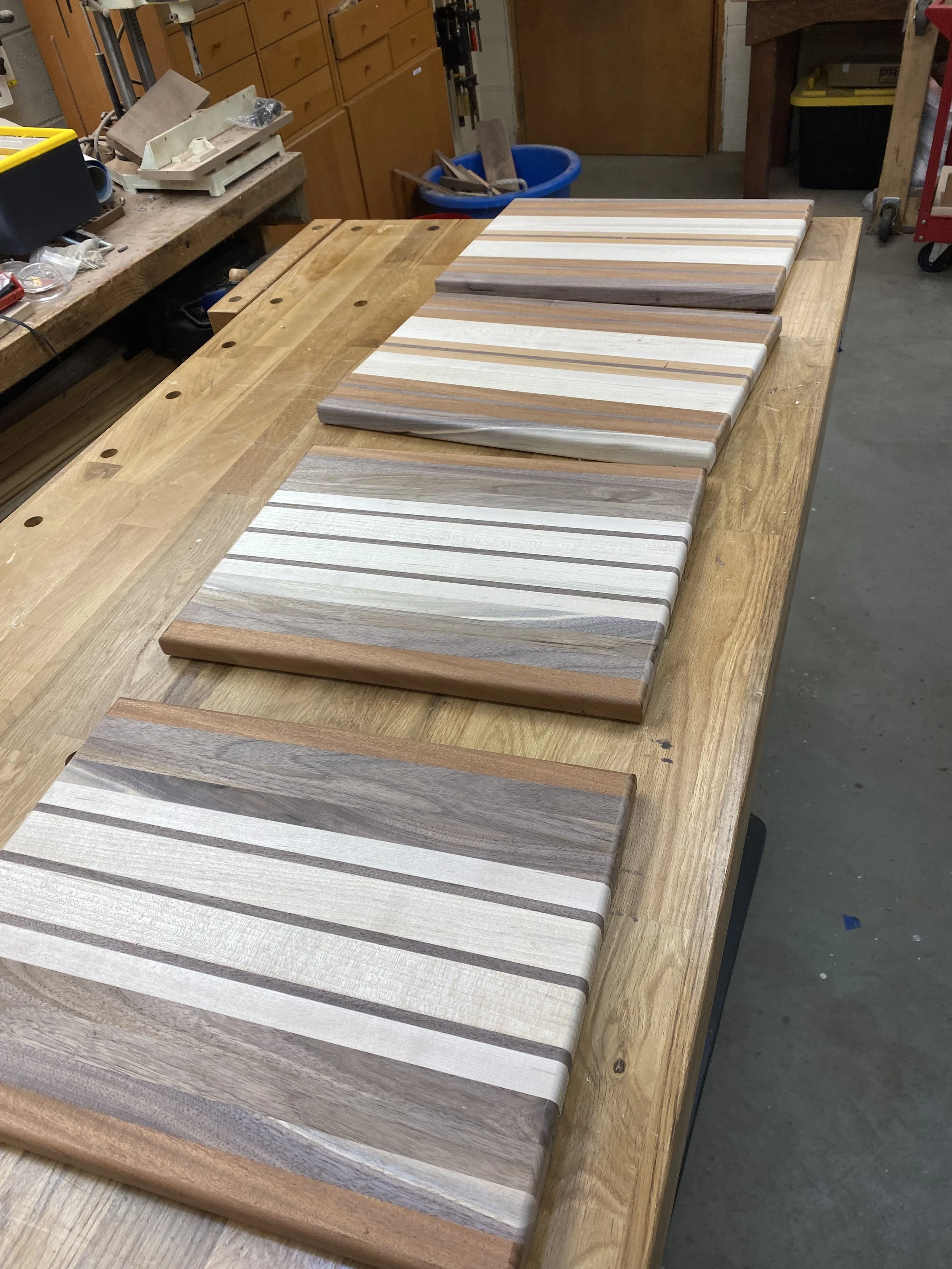 Several wooden cutting boards stacked on a workbench in a woodworking shop.