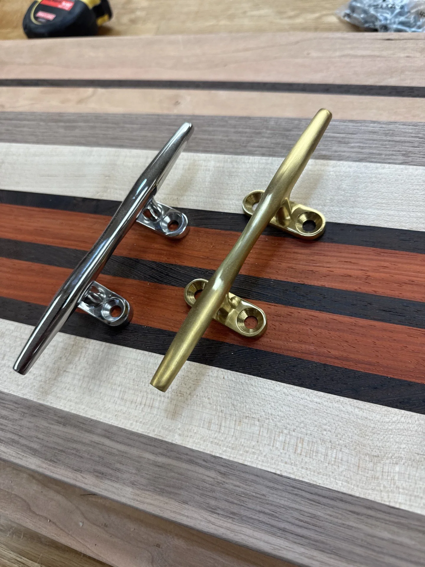 Two metal wall hooks, one in silver and one in gold, on a wooden surface with striped pattern.