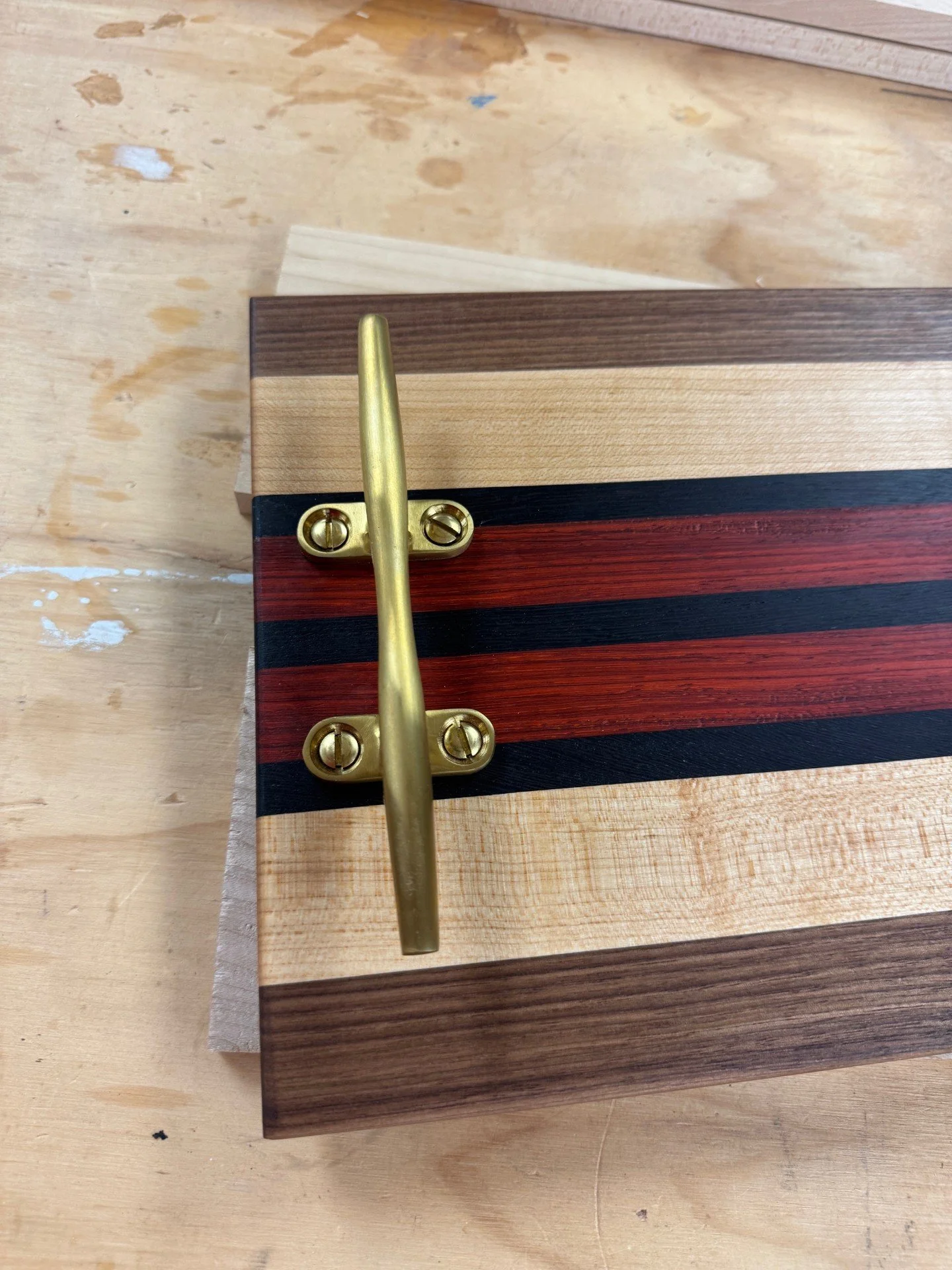 Close-up of a piece of wood with various colored inlays and a brass hinge and handle attached to it.
