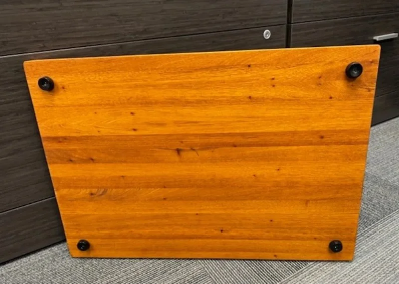 A wooden tabletop with four round black rubber feet, leaning against a dark brown cabinet on a gray carpet.
