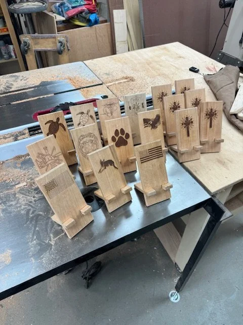 Multiple wooden plaques with engraved images of animals, nature scenes, and geometrical patterns, arranged on a work table in a woodworking workshop.