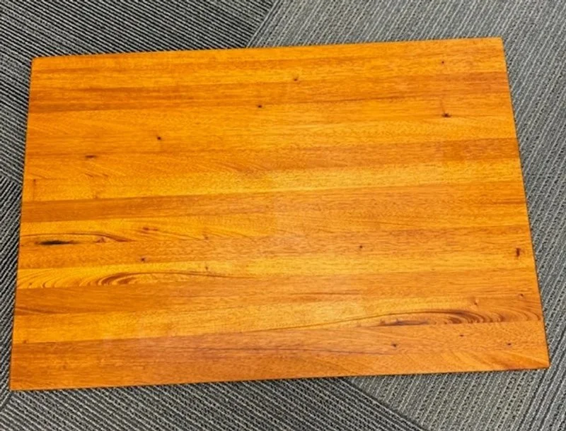 A wooden rectangular table top with a natural finish, placed on a gray carpeted floor.