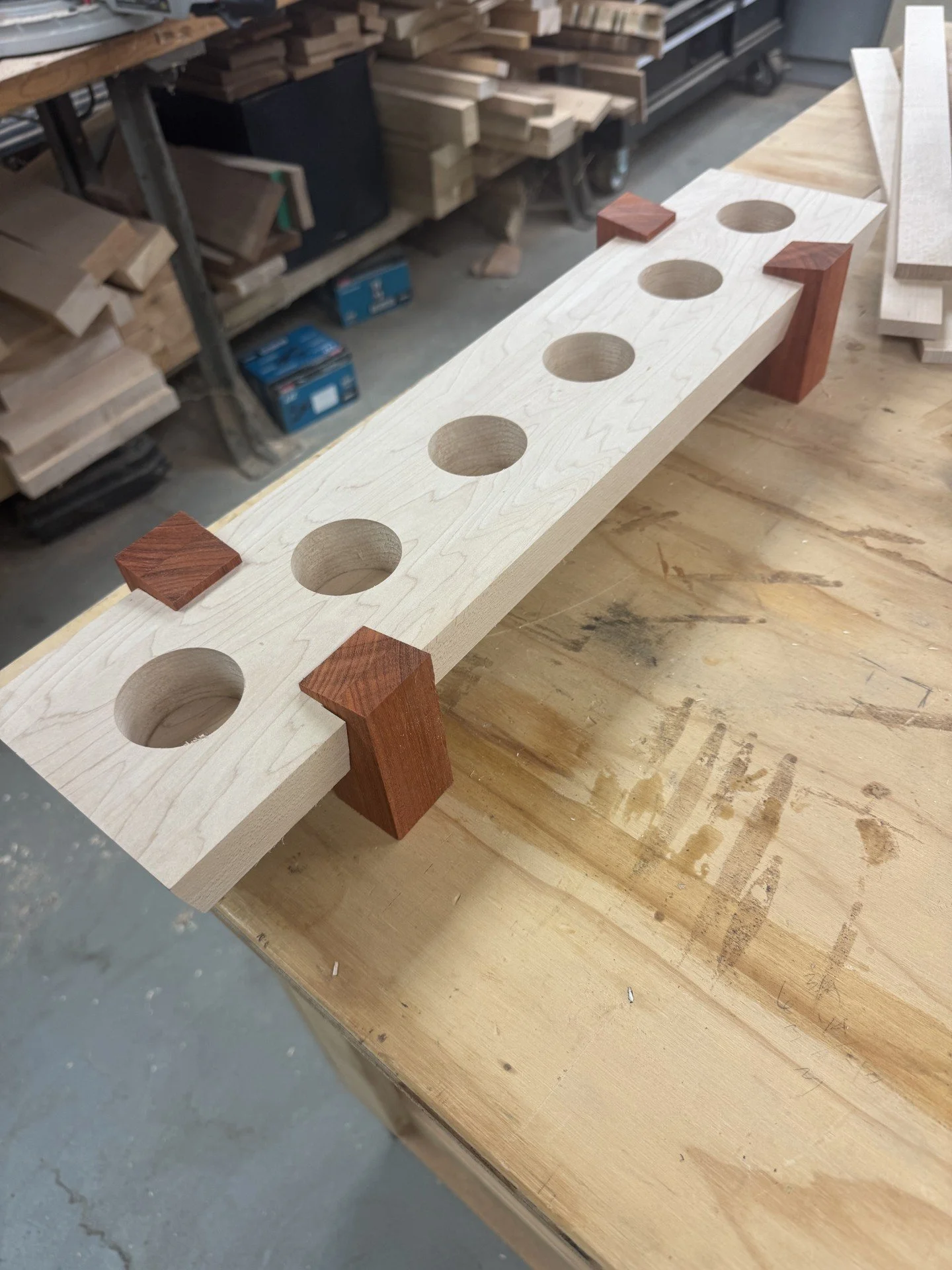 A wooden board with drilled holes and wooden blocks on a workbench in a woodworking shop.