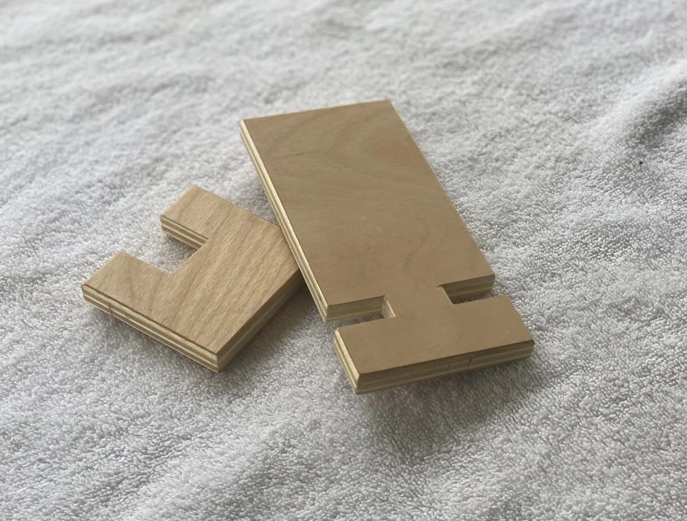 Two wooden pieces with cutouts, one large and one small, placed on a textured white surface.