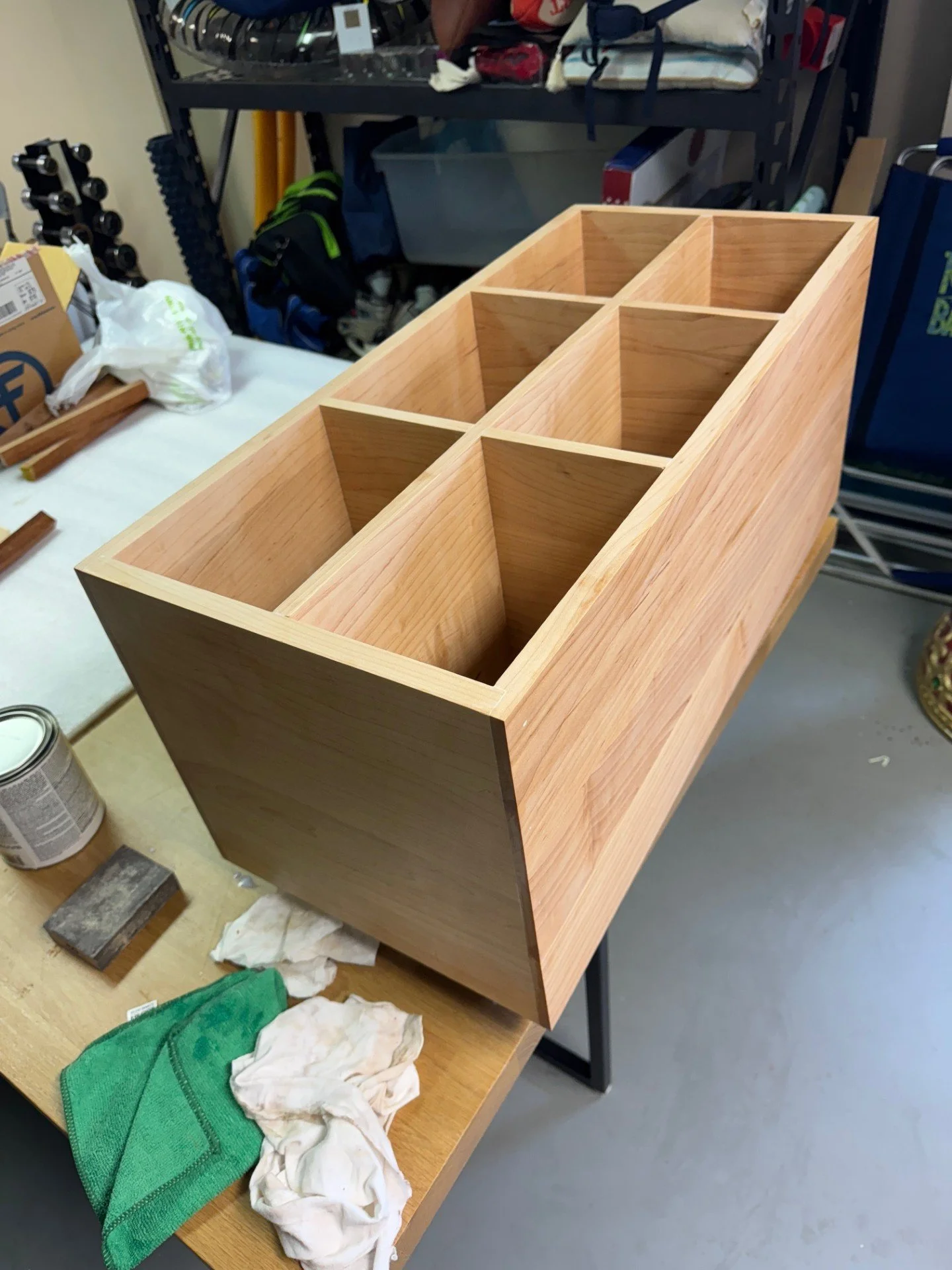 A wooden organizer with eight compartments on a workbench in a garage or workshop setting, surrounded by tools, cleaning cloths, and small cans.