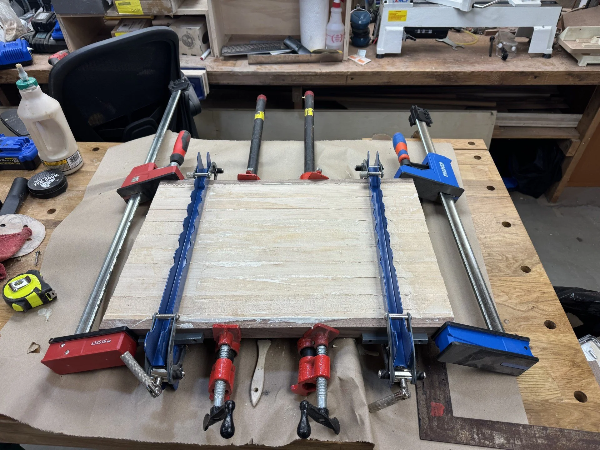 Clamps holding a piece of wood on a workbench in a woodworking shop.