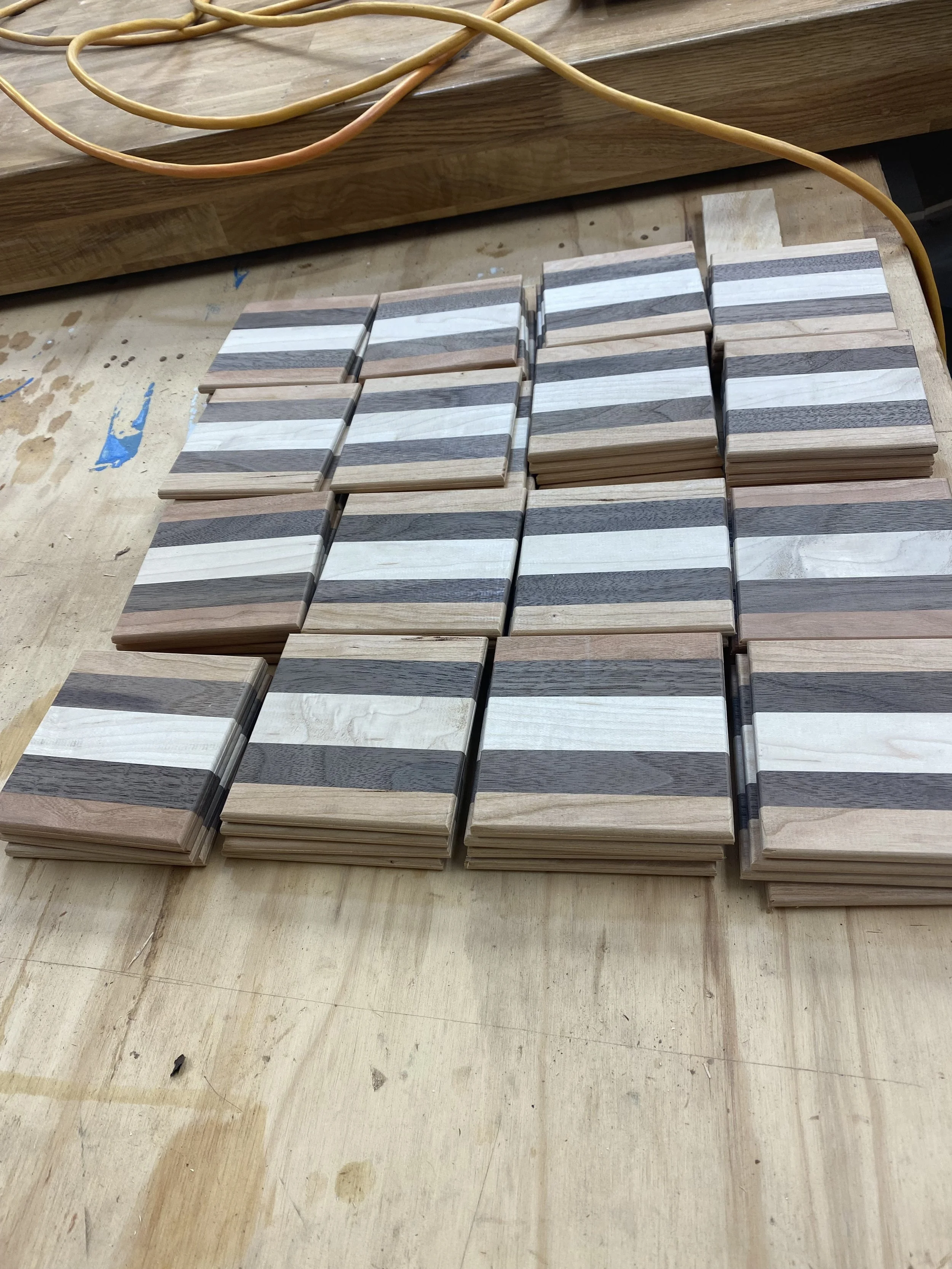 Stacks of small, rectangular wooden tiles with alternating light and dark wood grain patterns on a light-colored wooden work surface.