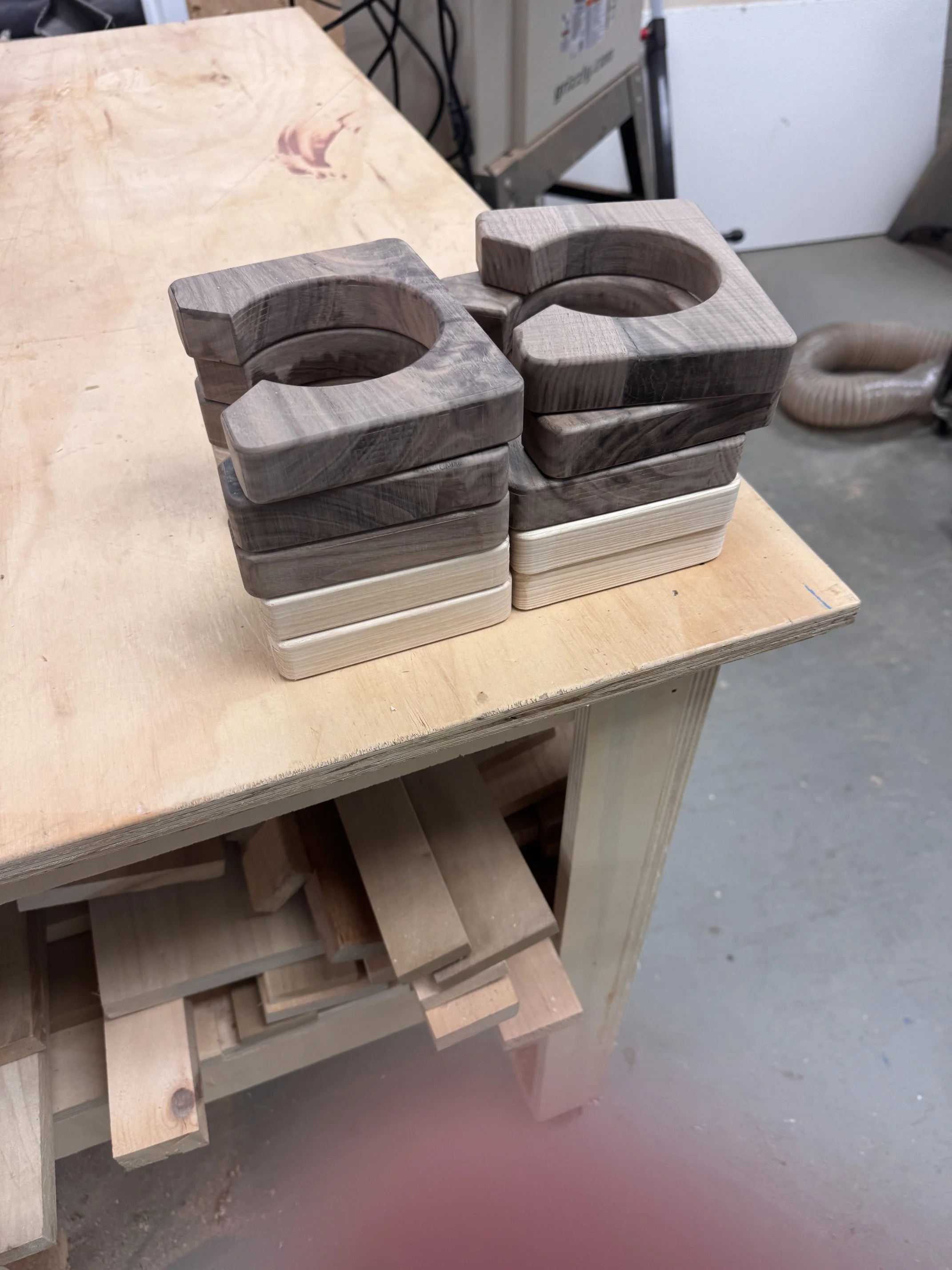 Stacked wooden objects with circular cutouts on a workbench in a woodworking shop.
