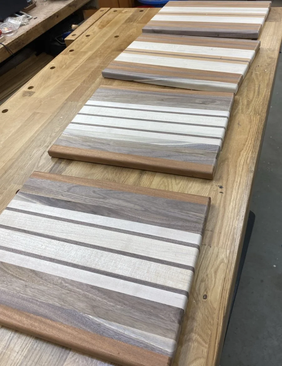 Wooden cutting boards with striped patterns laid on a workbench in a woodworking shop.