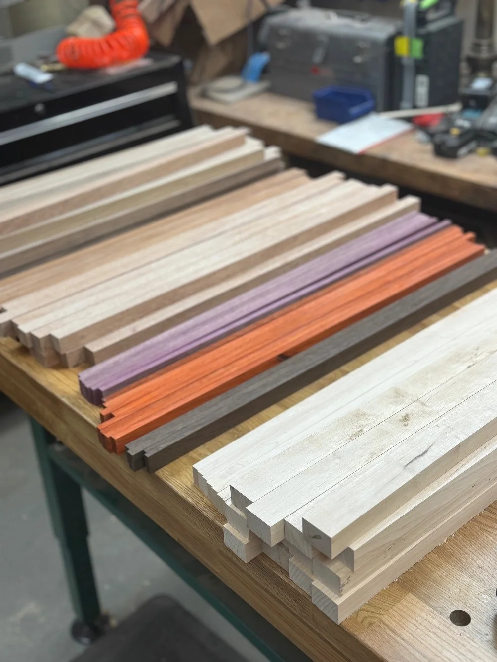 Various wooden strips in natural, painted, and stained colors laid out on a workbench in a woodworking shop.