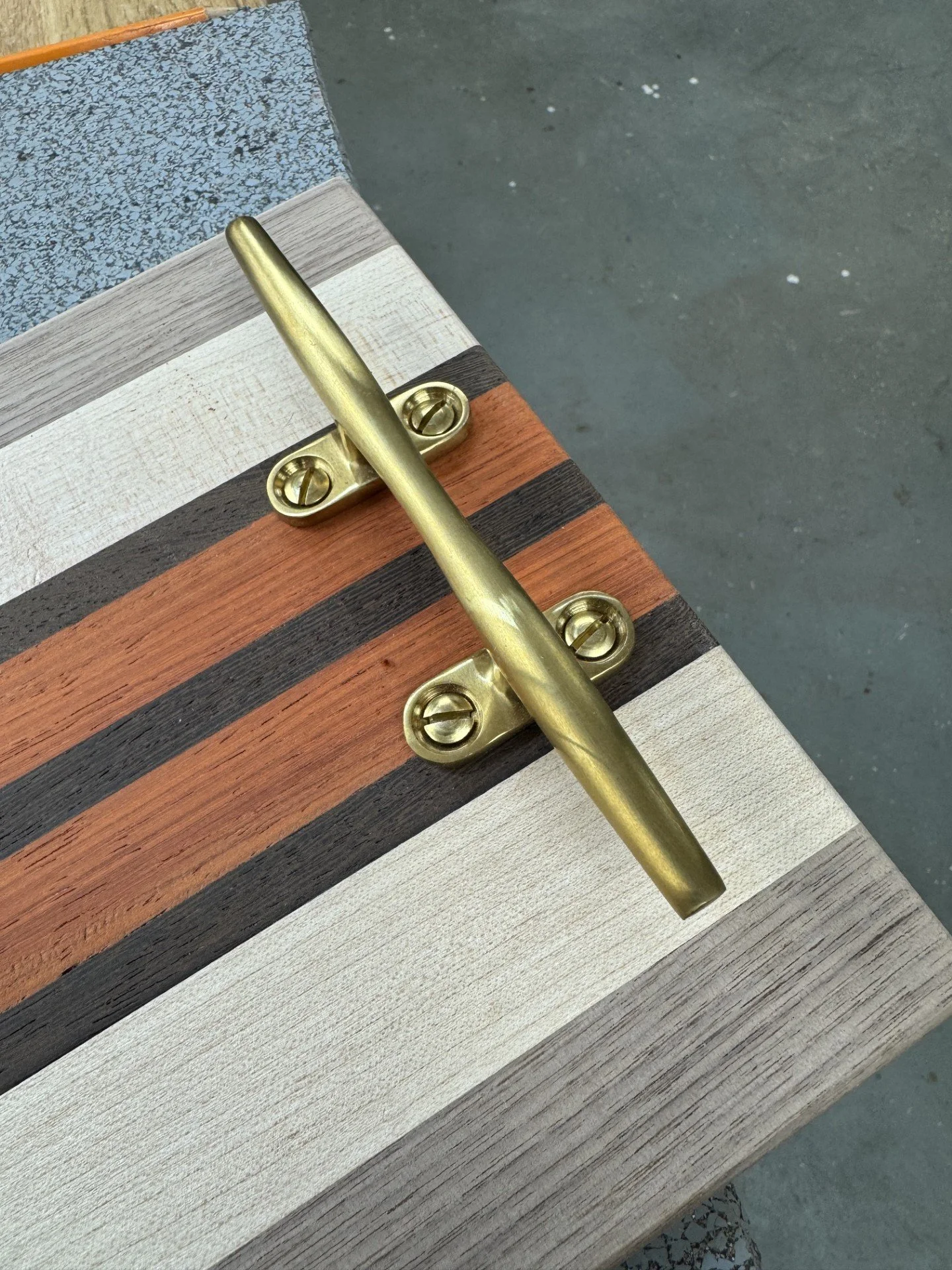 Close-up of a brass handrail attached to a surface made of horizontal wooden slats in different colors.