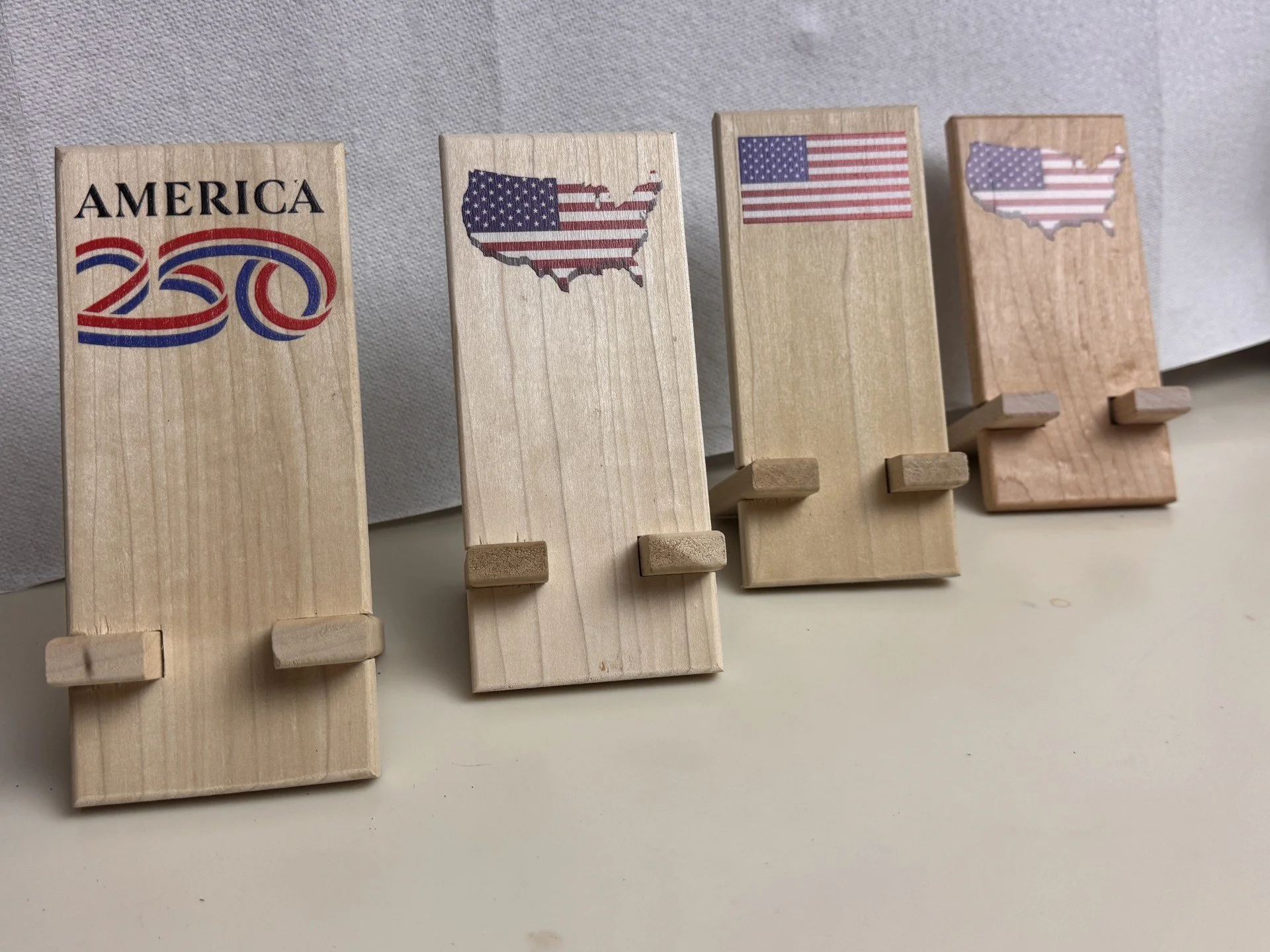 Four wooden blocks with American flag designs and shapes of the United States, arranged in a row on a beige surface.