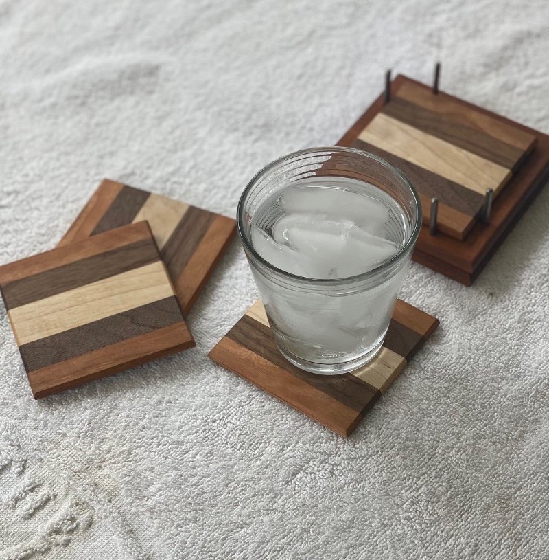 A glass of water with ice cubes on a wooden coaster, placed on a textured white surface, with additional wooden coasters nearby.