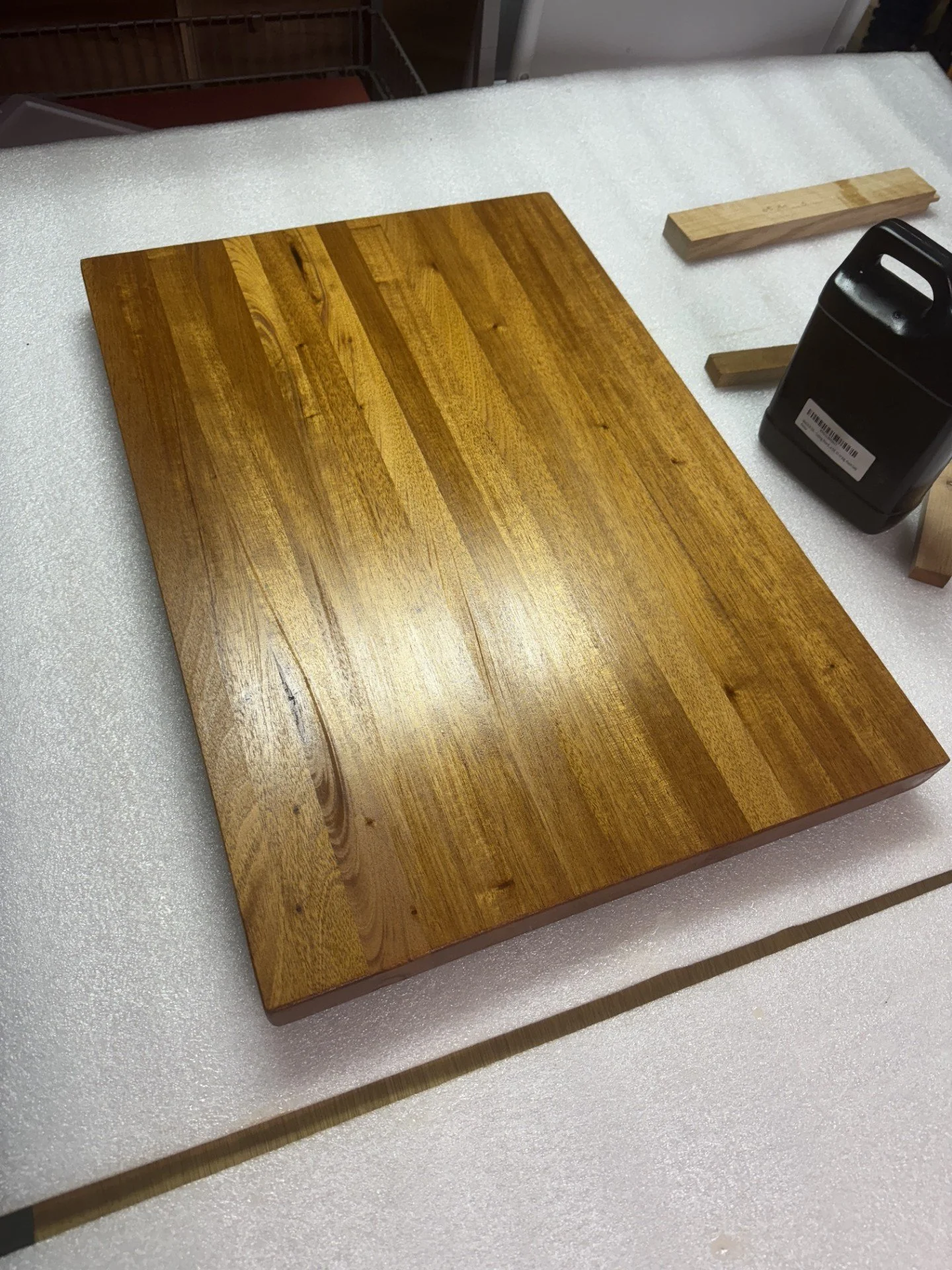 Two pieces of wood, one larger and one smaller, on a white foam surface, with a black container nearby.
