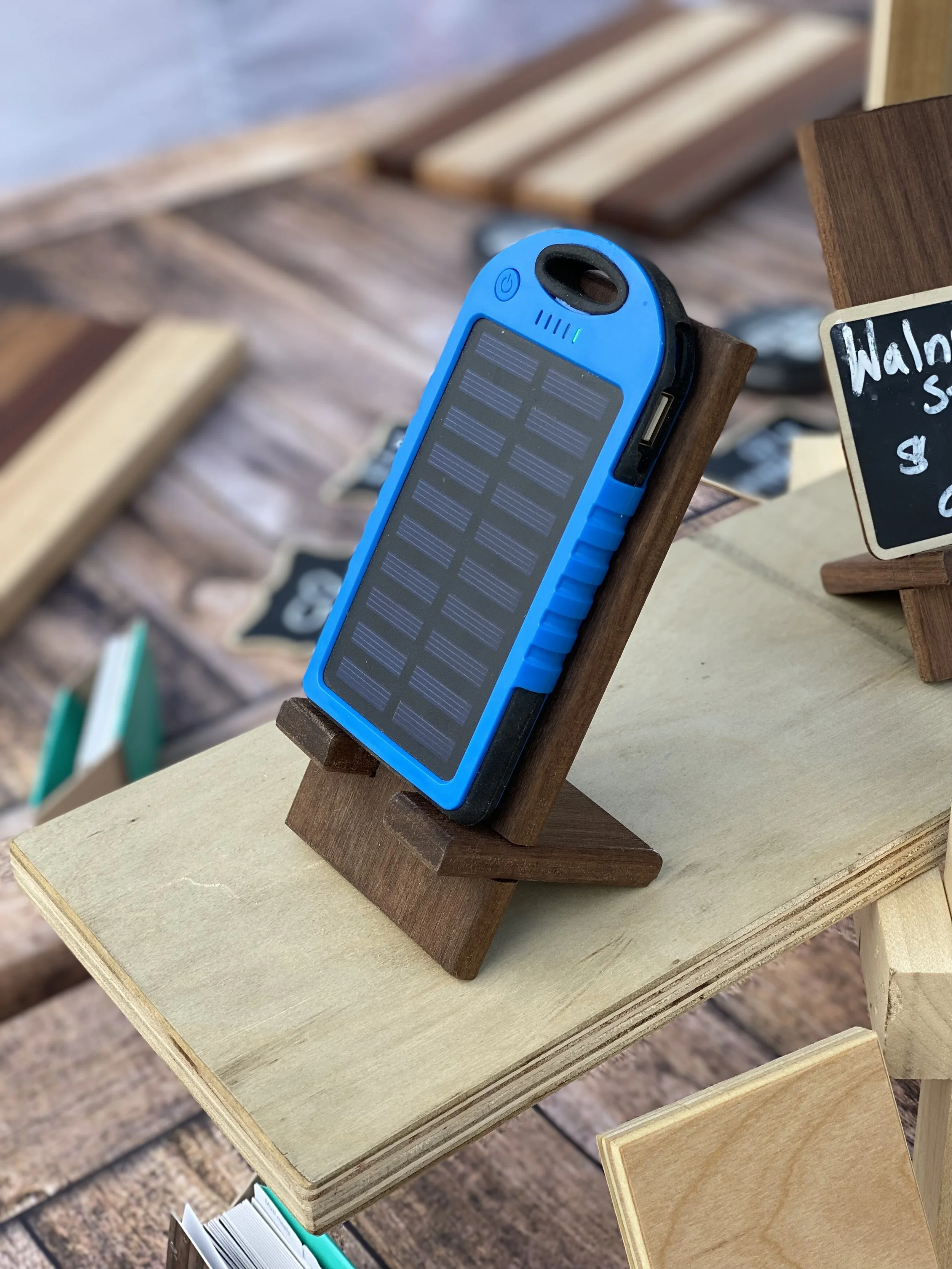 A small portable solar power bank with a blue frame and solar panel, displayed on a wooden stand at an outdoor market.