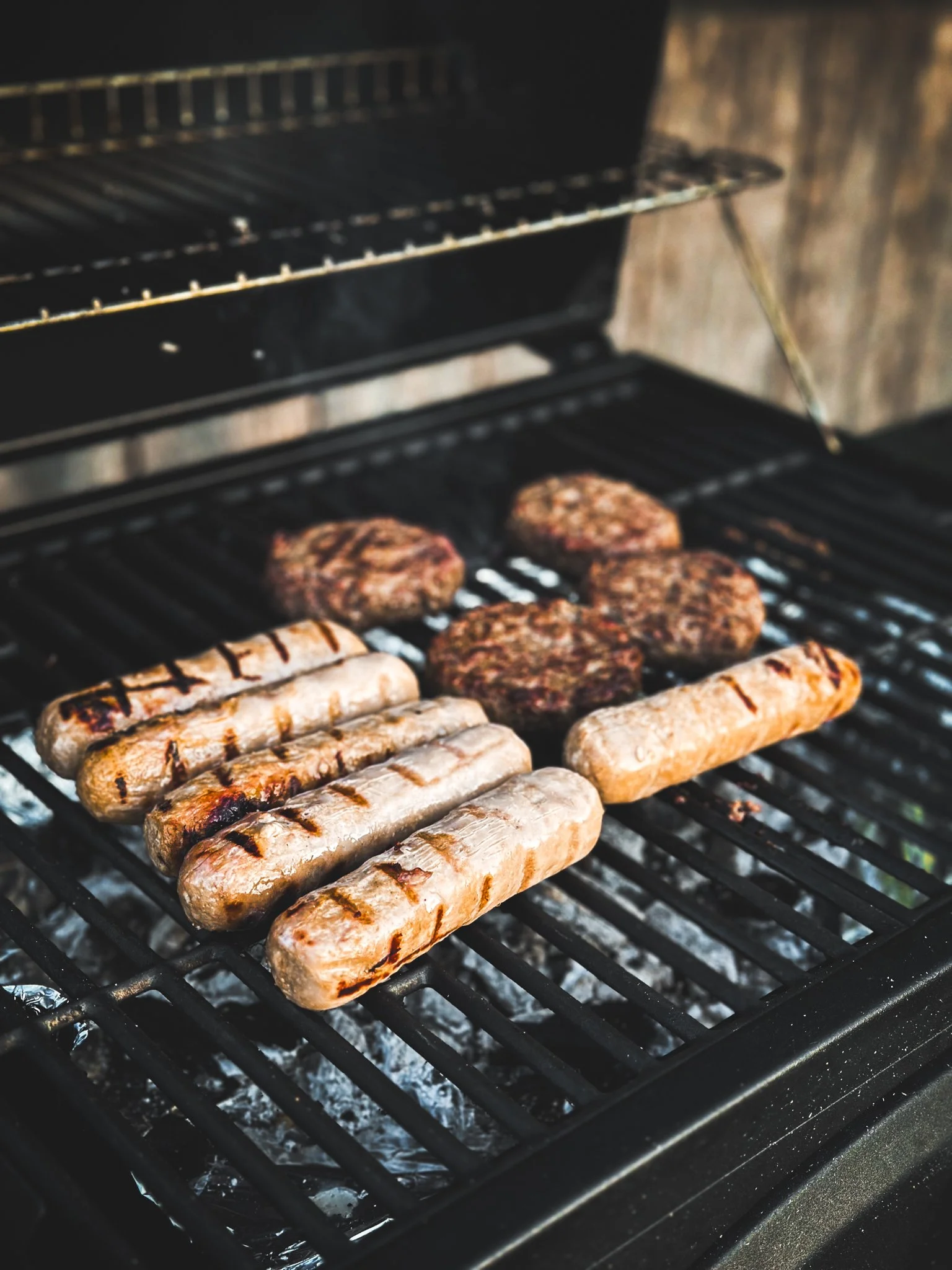 Sausages and hamburger patties cooking on a barbecue grill.