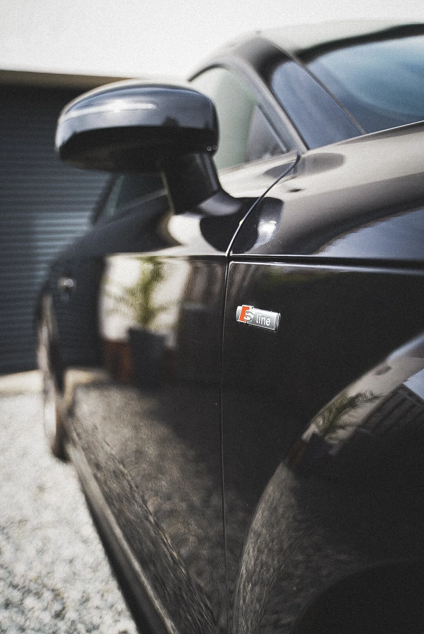 Close-up of a black car door with a side mirror, a daytime setting, and a sticker that reads 'S line' on the side of the vehicle.