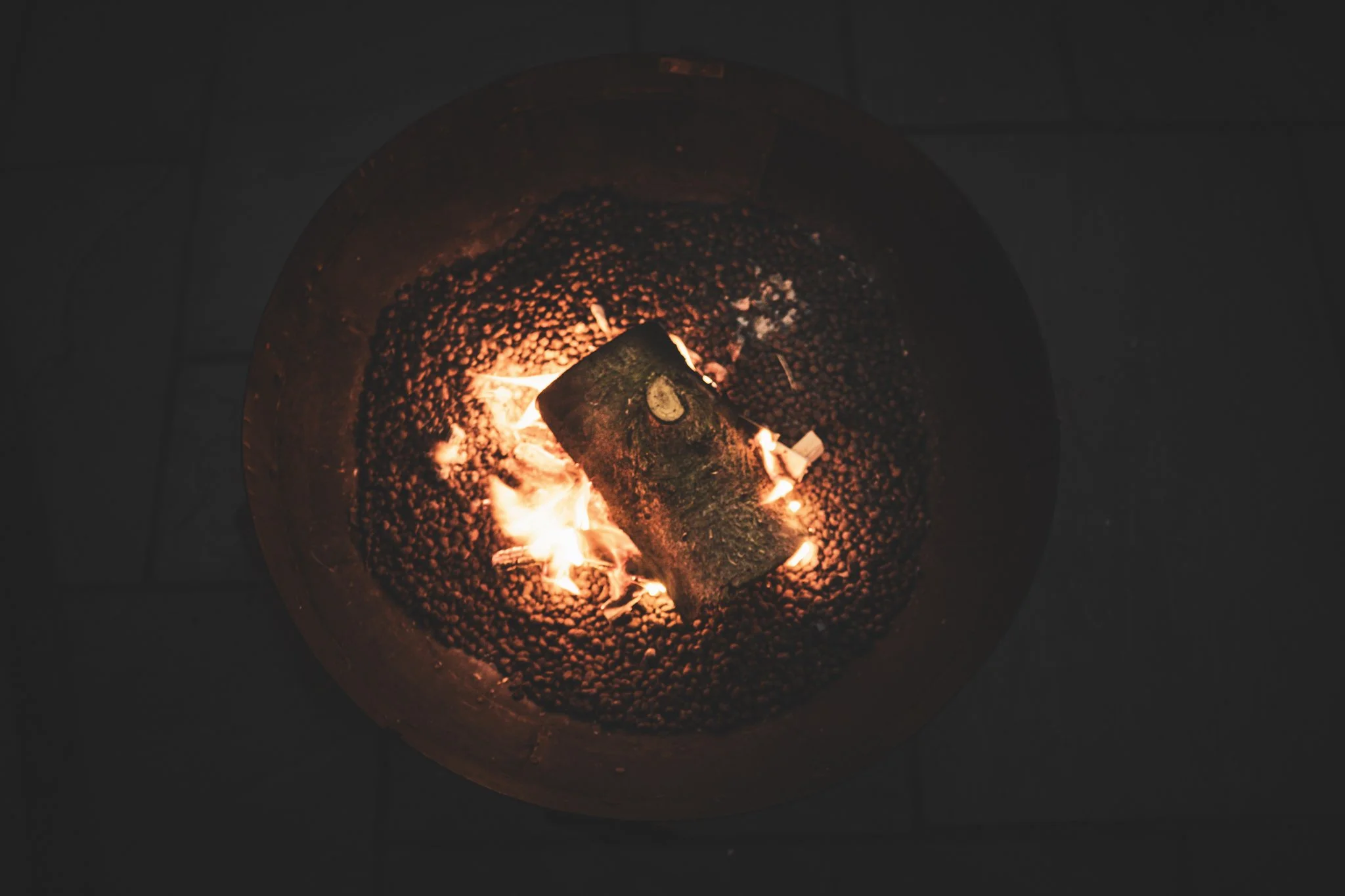 Burning piece of wood inside a fire pit with glowing embers and flames.