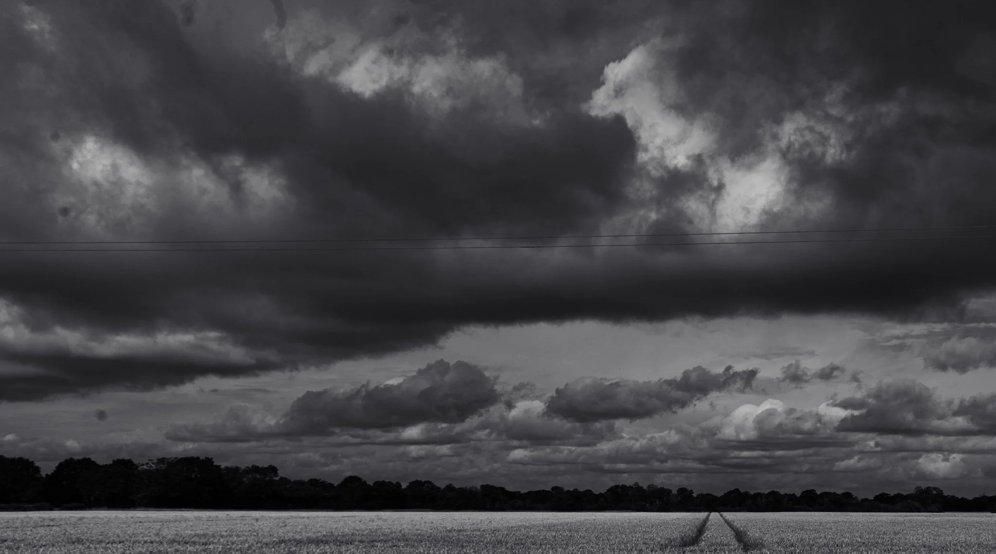 Dark, cloudy sky over a rural landscape with trees and an open field.