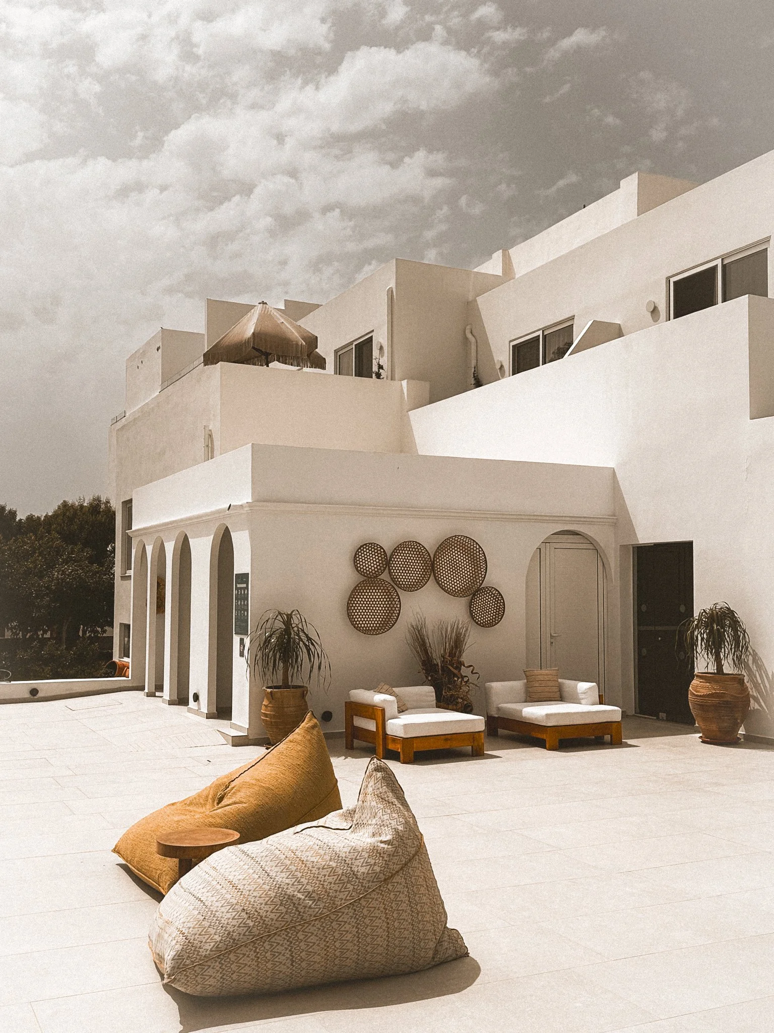Outdoor patio area with beige cushions, wicker planters, and decorative wall art on white building facade.