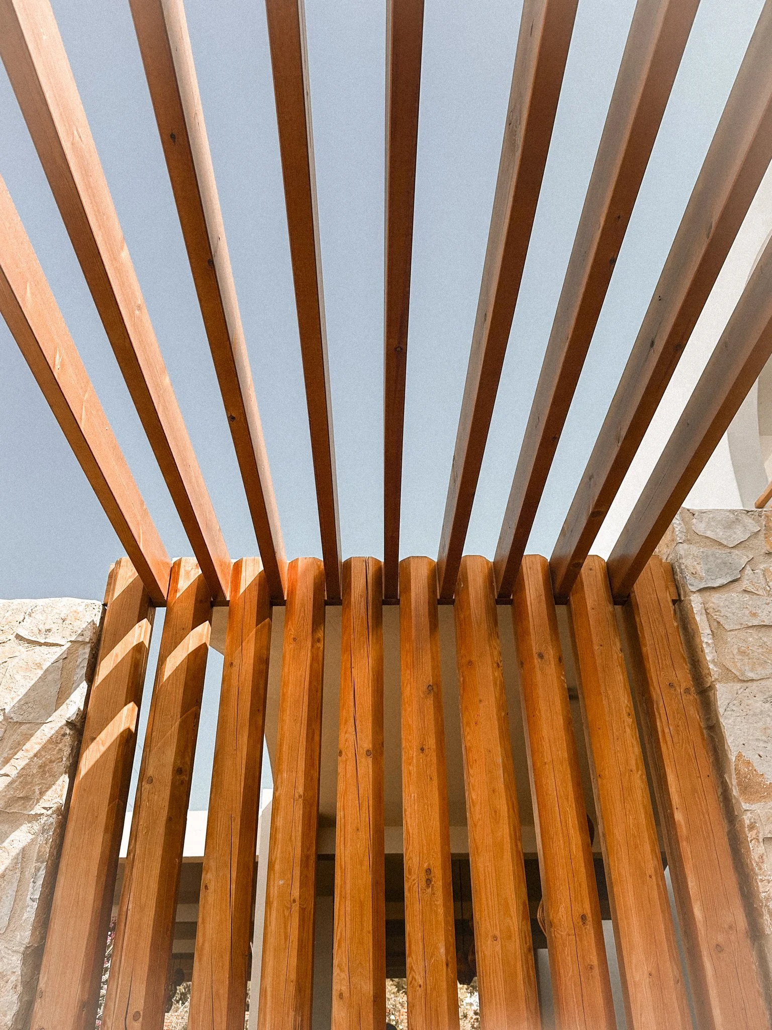 Wooden slats or beams arranged vertically with a blue sky in the background and part of a stone wall visible on the sides.