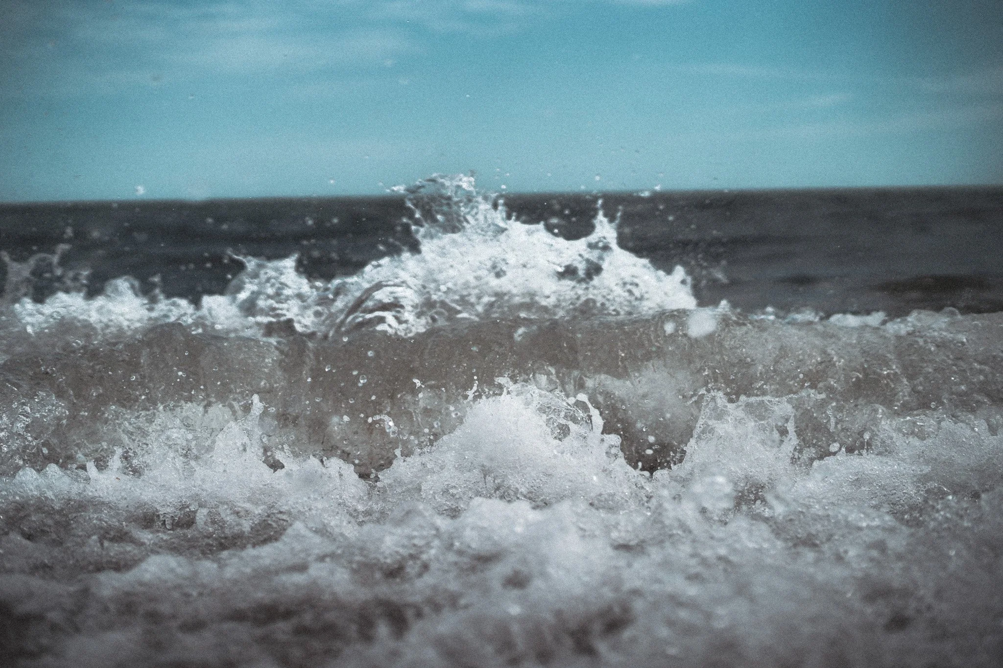 Waves crashing onto the shore on a clear day with blue sky.