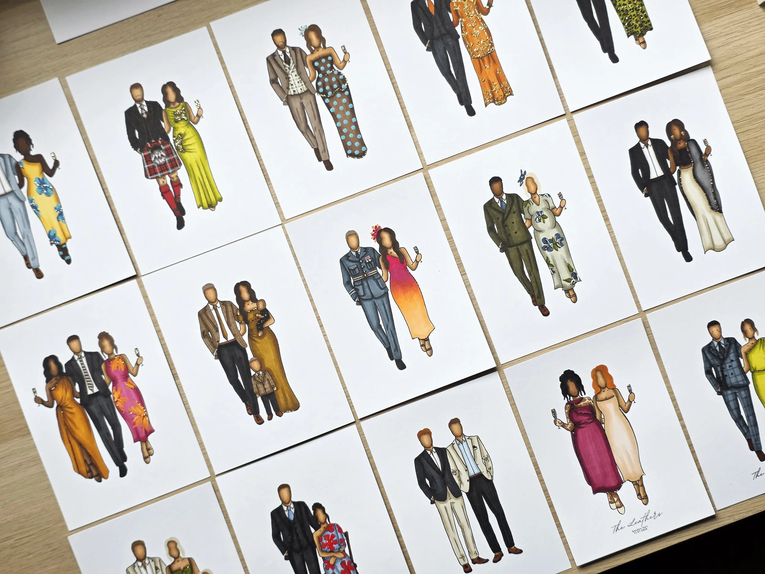 Multiple illustrated paper cutouts of couples in formal and glamorous attire, some holding wine glasses, laid out on a wooden surface.
