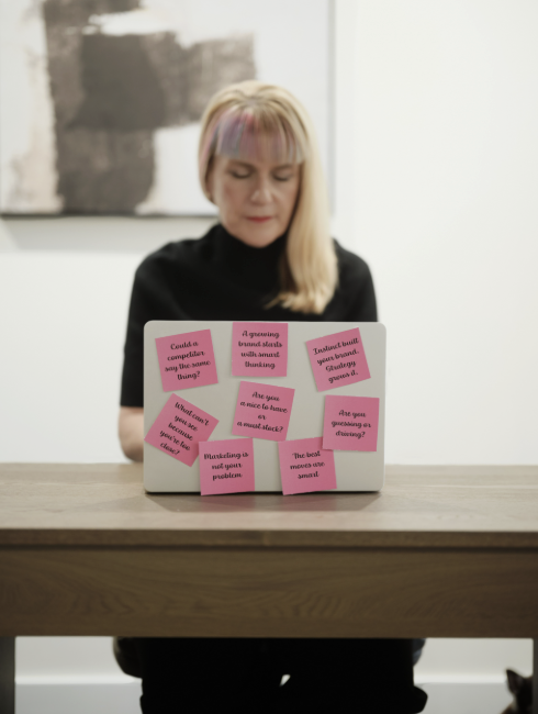 Woman with blonde hair and pink streaks working on a laptop covered with pink sticky notes in a modern room.