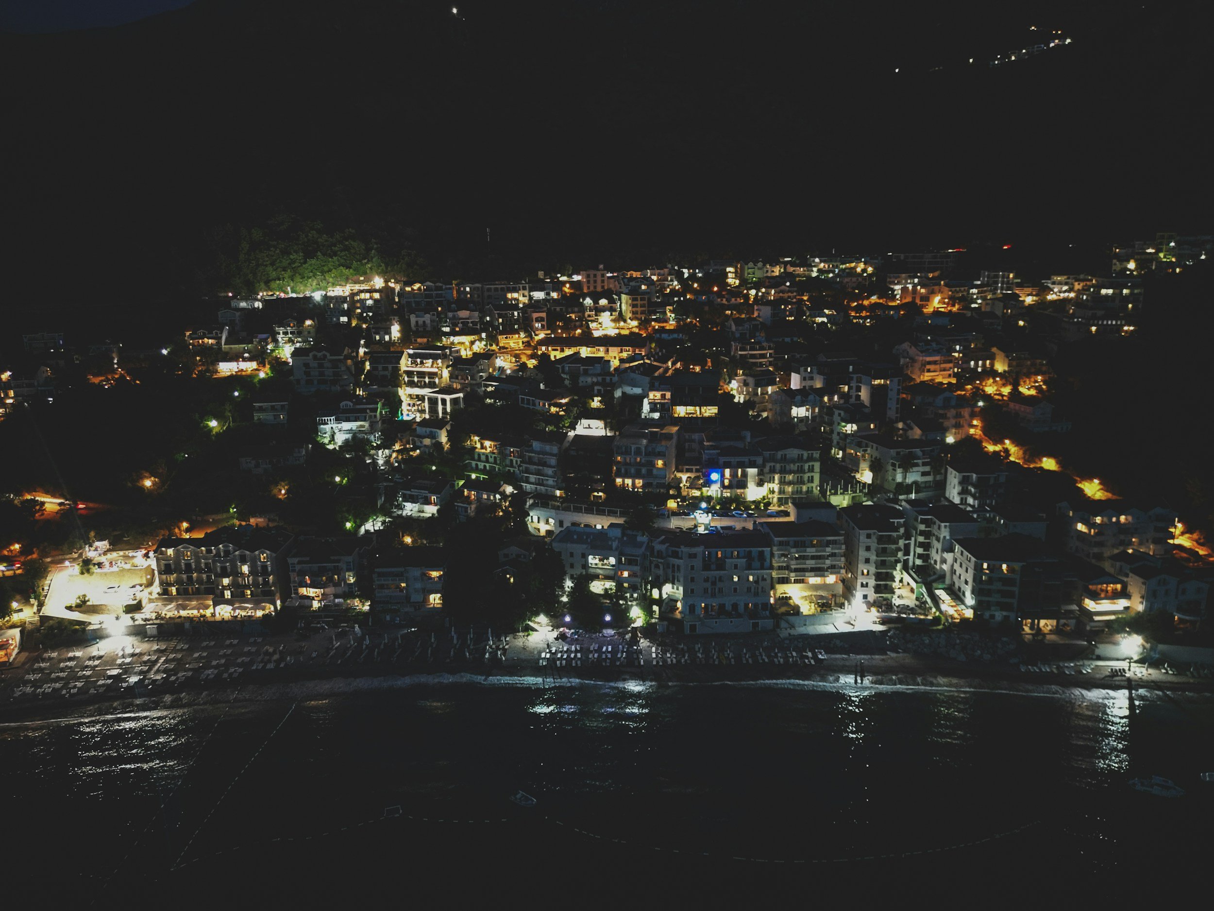 Night view of a coastal city with many illuminated buildings and streets, seen from the water.