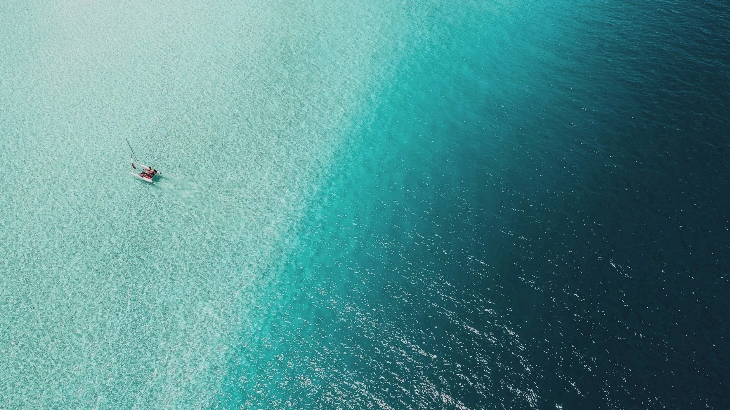 An aerial view of a boat sailing in clear turquoise water.