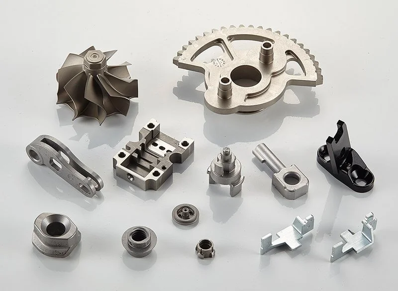 Various metallic mechanical parts, including a turbine wheel, gear, brackets, and fasteners, arranged on a white surface.