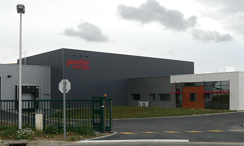 Industrial building with a black facade and red signage reading 'pourite europe,' with a fence, stop sign, and cloudy sky in the background.