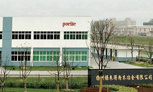Exterior view of a factory building labeled 'porite' with trees and a grassy area in the foreground.