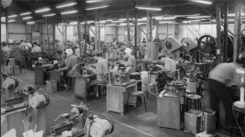 Workers operating machinery in a large factory or workshop setting.