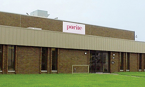 Exterior view of a brick building with a large sign that reads 'porite' on the upper facade, and a well-maintained grassy area in front.
