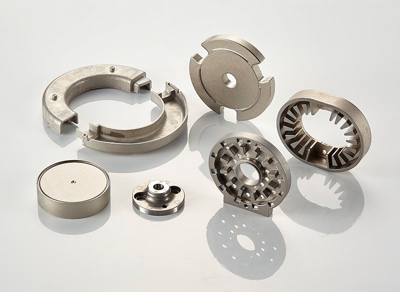 Various metallic mechanical parts, including circular and ring-shaped components, arranged on a white surface.