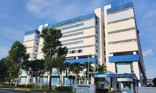 Large modern hospital building with a sign that reads Panotech, surrounded by trees and a clear blue sky.