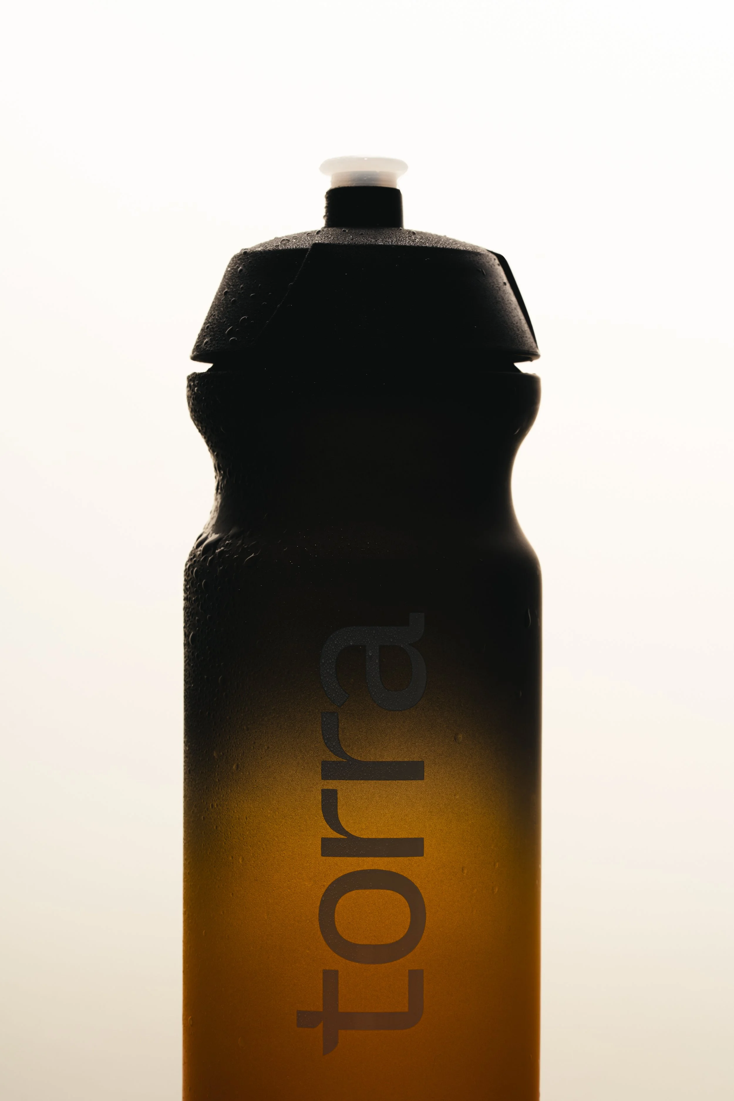 Close-up of a bottle with a yellow bottom and black upper part, bottle cap on top, covered in water droplets, with the word 'tr...'
