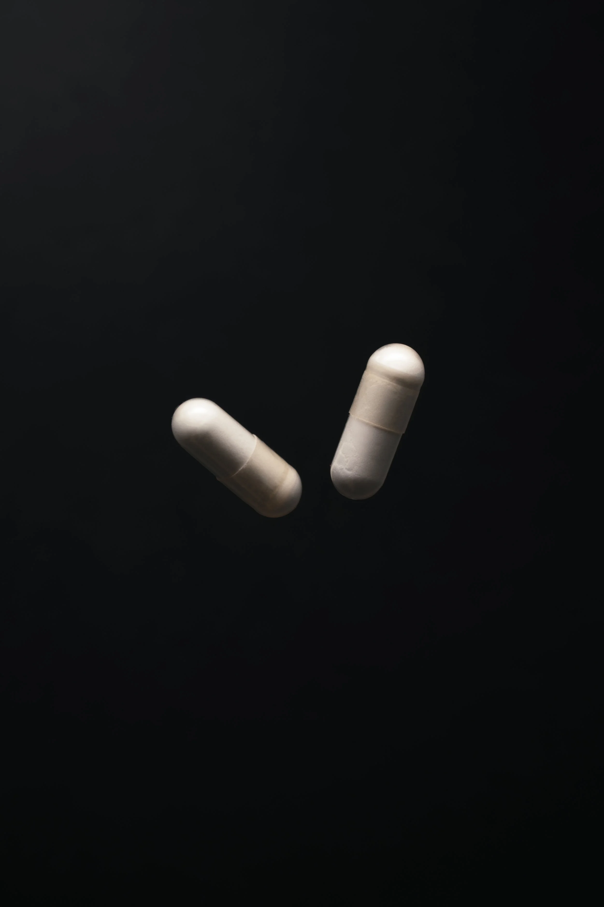 Two white capsules on a black background.