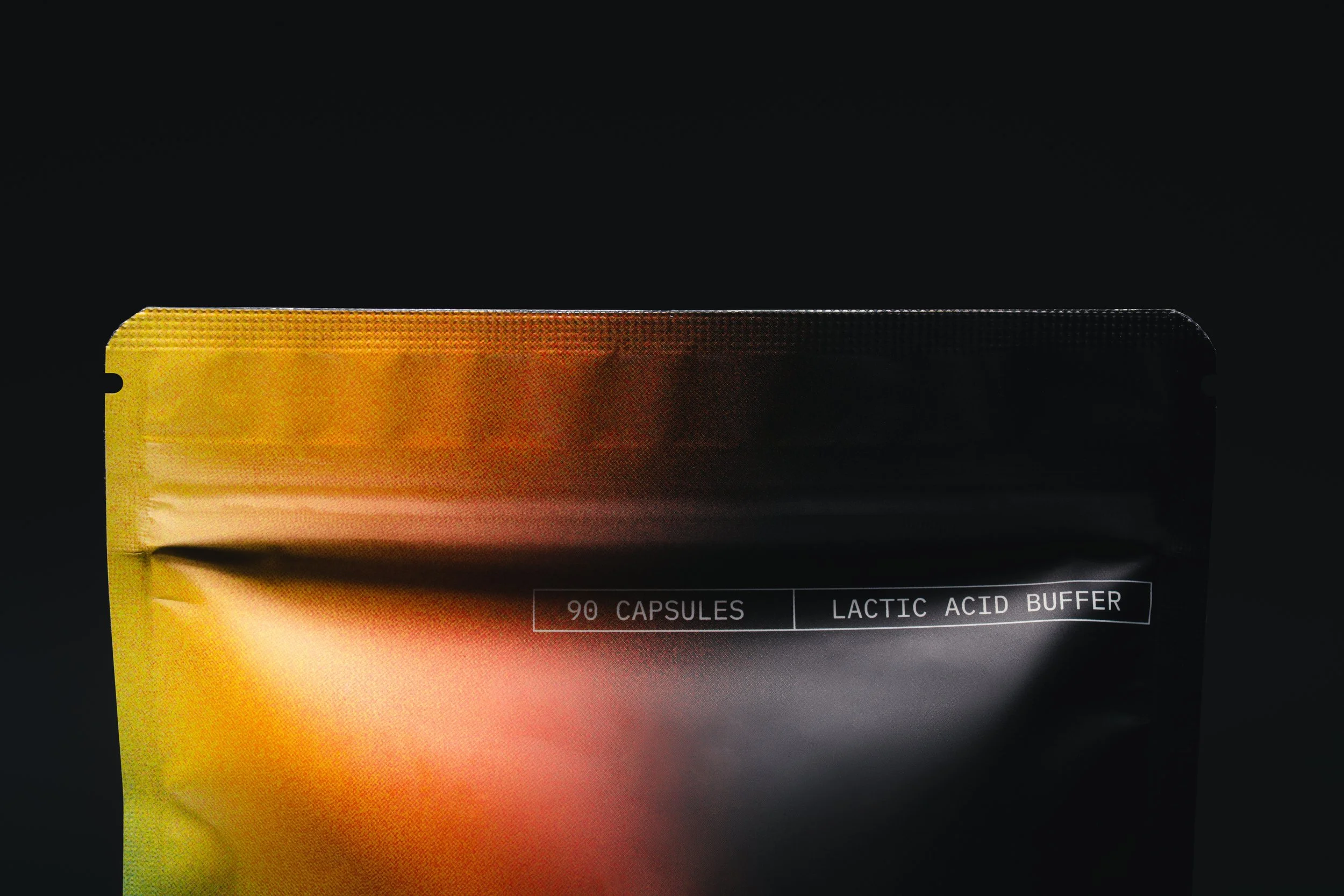 Part of a black box of dietary supplement capsules with yellow and orange gradient packaging, indicating 90 capsules, with text stating 'Lactic Acid Buffer'.
