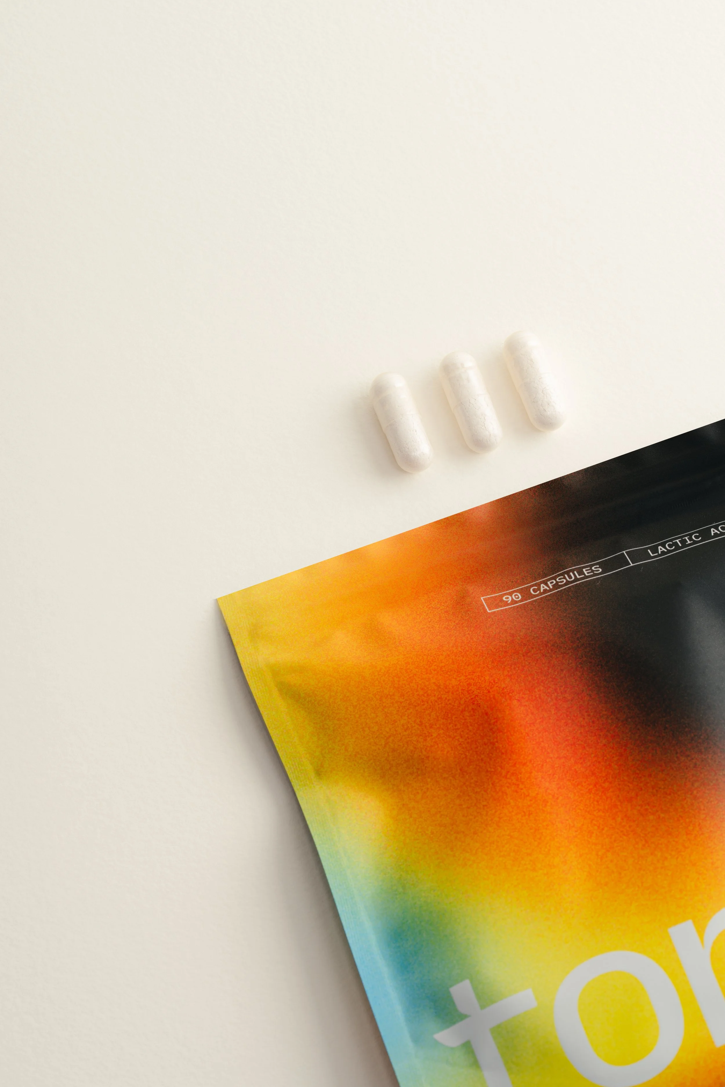 Three white capsules on a white surface near a colorful box.