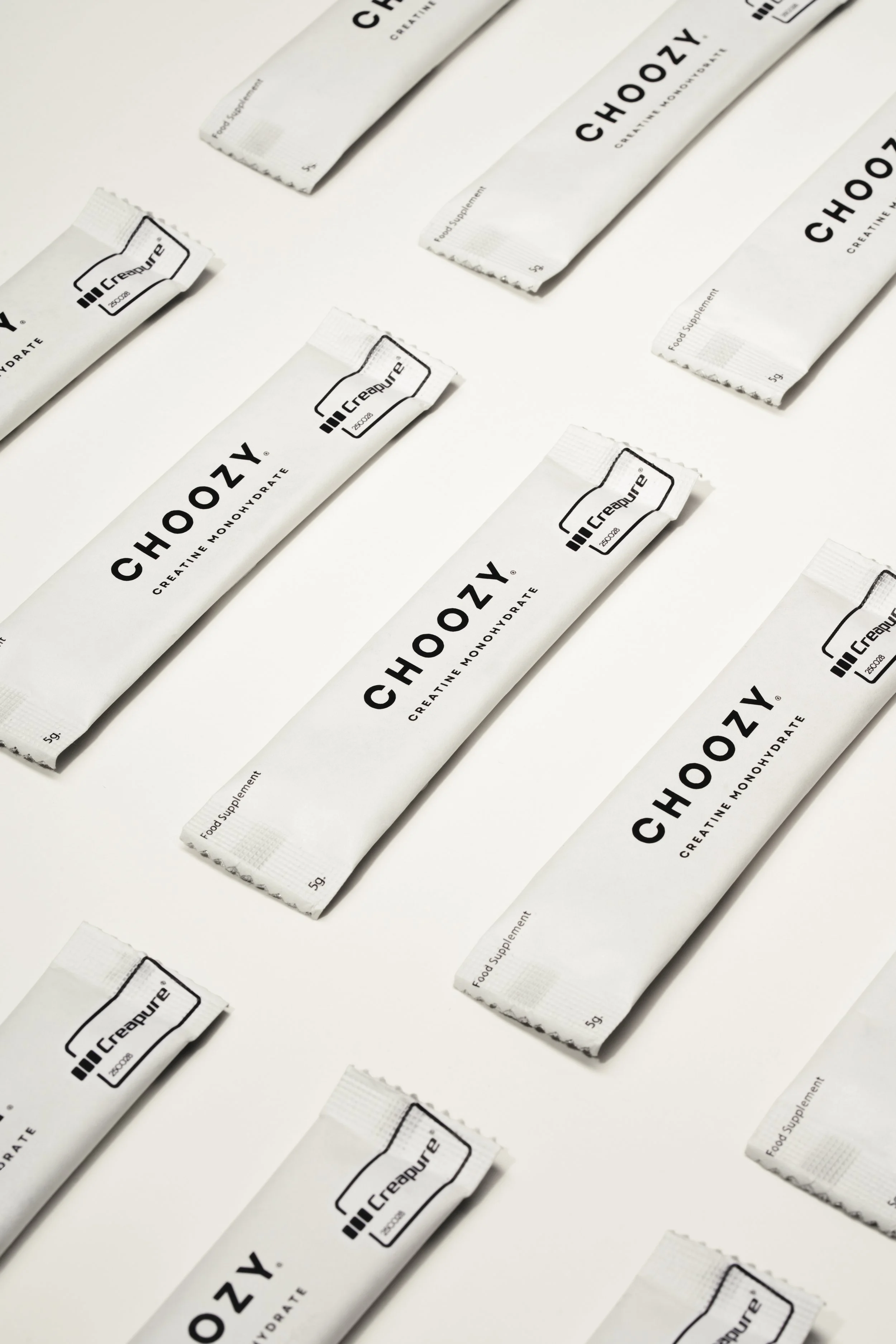 Multiple white packets of creatine monohydrate dietary supplement arranged in rows on a white background.