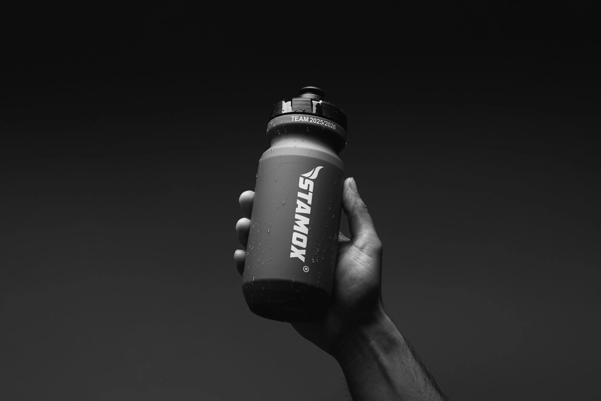 A hand holding a water bottle with condensation droplets, against a dark sky background.
