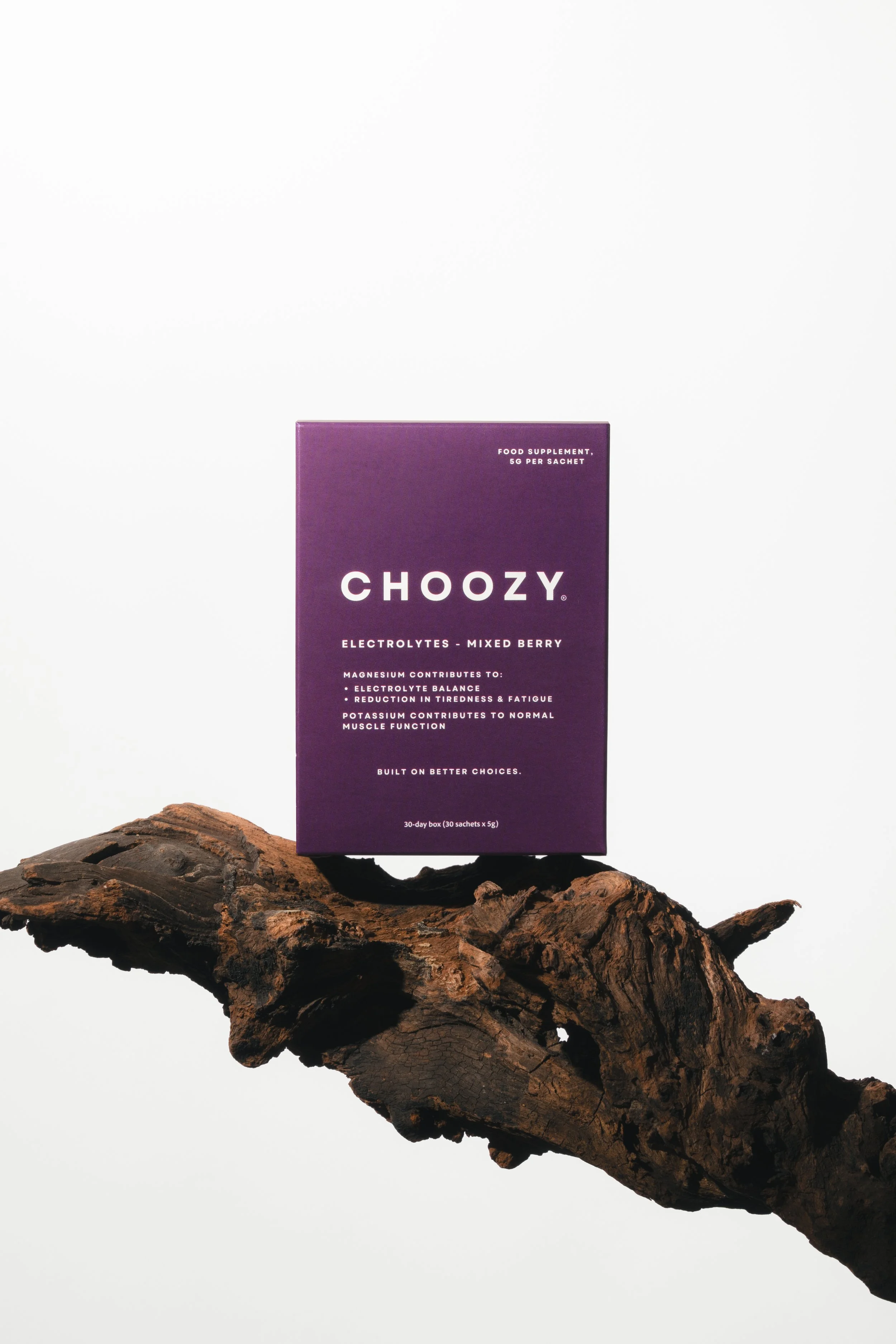 A purple box of Choozy electrolyte supplements placed on a large piece of dark, textured wood against a plain white background.