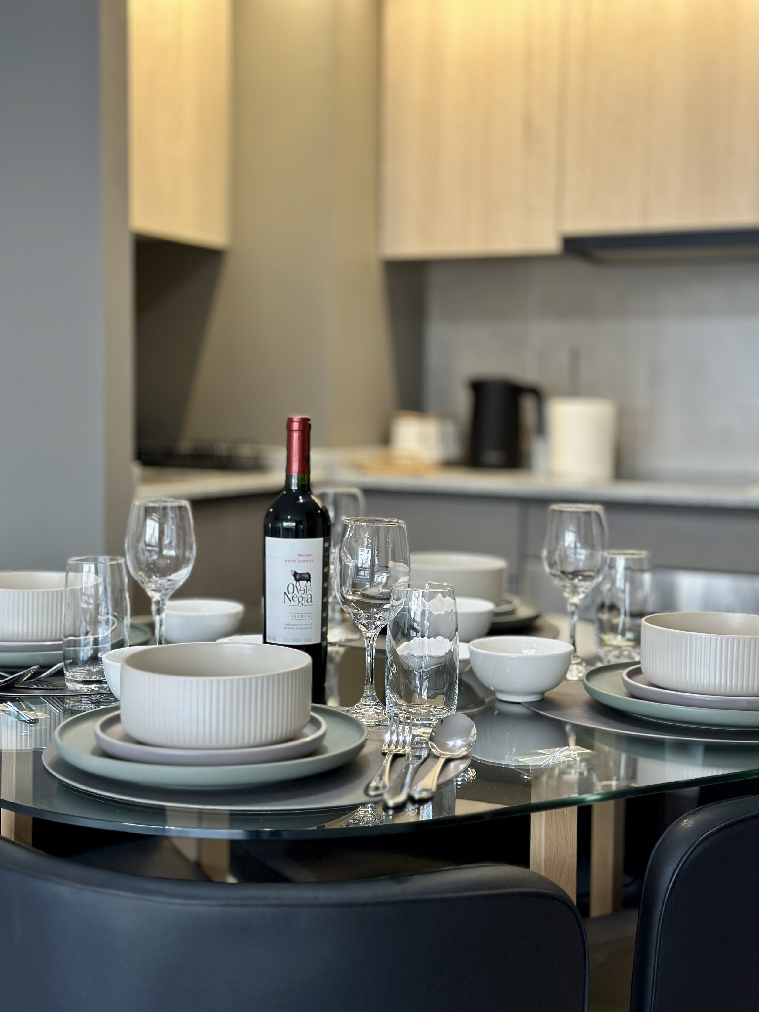 Mesa puesta para una comida con platos, copas, cubiertos y una botella de vino, en un ambiente moderno de cocina o comedor.