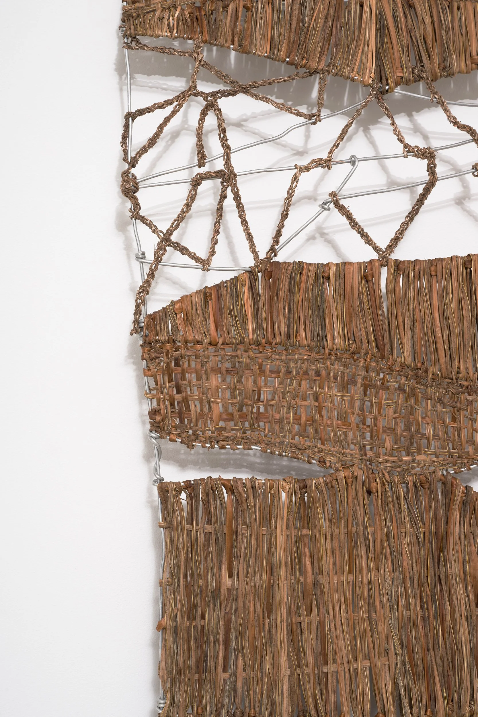 Close-up of woven brown baskets hanging on a metal wire rack, with a white wall in the background.