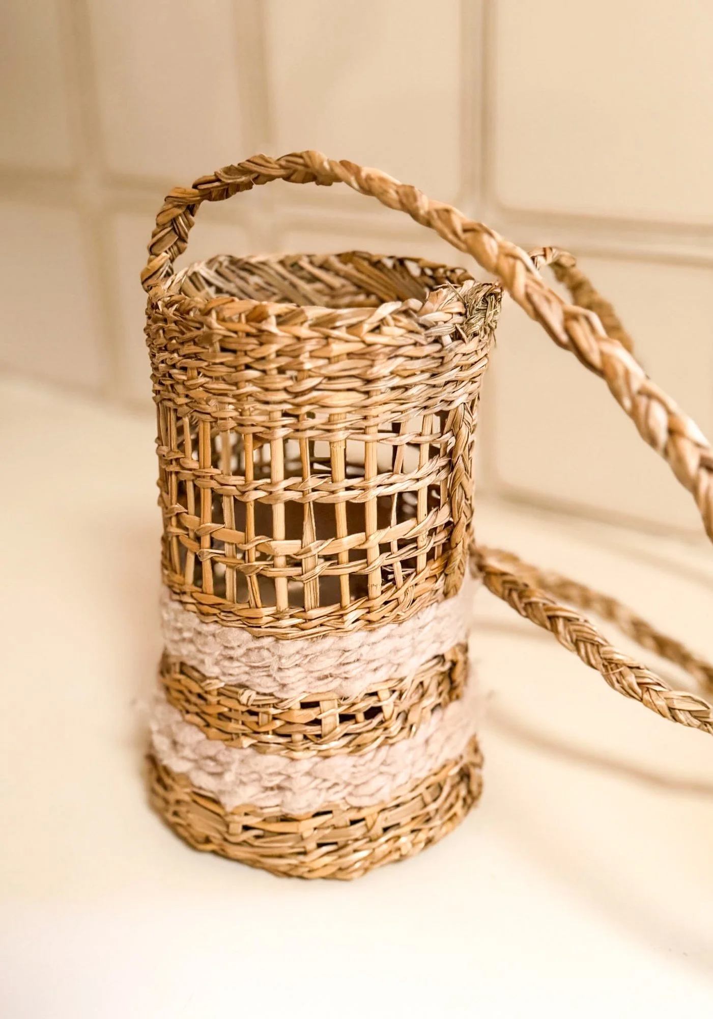Twined woven baskets made of natural fibres, with a plaited rope as handle, set against a neutral background.