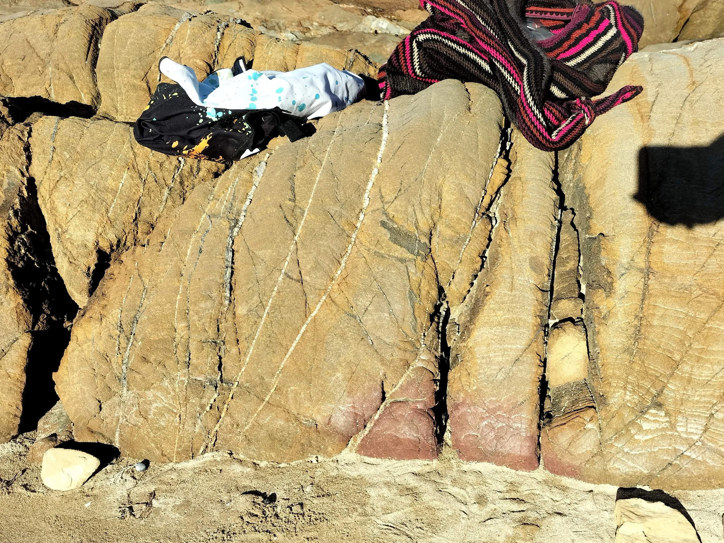 Close-up of layered rocks with a black, colorful scarf and a white cloth with blue and yellow paint splatters resting on the rocks.